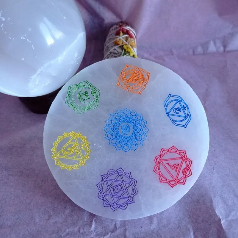 BASE REDONDA DE PIEDRA SELENITA CON TAMAÑO APROXIMADO DE 12 CM CON SÍMBOLOS DE LOS 7 CHAKRAS